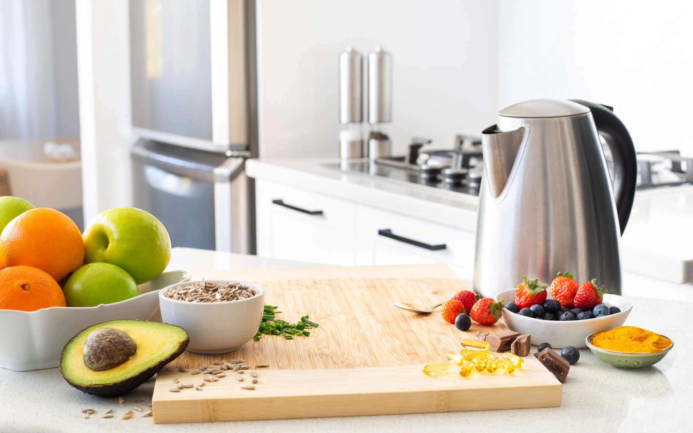 Kitchen setting with kettle, bowl of fruit, seeds, spices and supplement pills